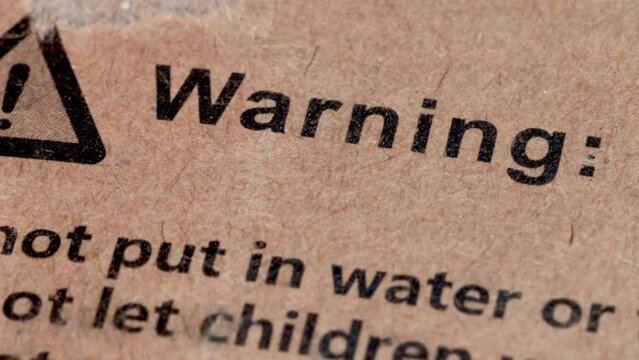 Warning sign on the cardboard surface of a box, waning text in the paperboard of the box of a product macro shot in close up view.