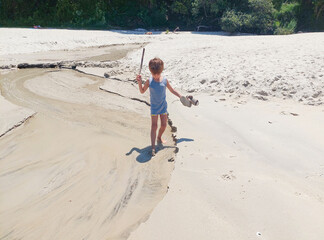 little boy playing on the beach with a pirate sword