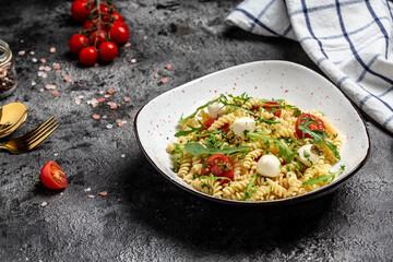 Italian cold pasta salad. Fusilli, tomato, mozzarella, olive, arugula. Pasta alla caprese on a dark background, Restaurant menu, dieting, cookbook recipe top view