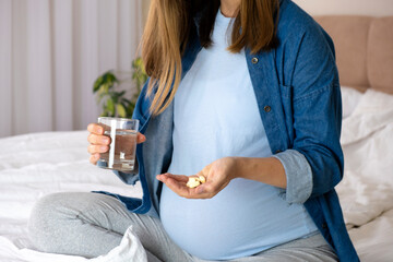 Pregnant woman hold pills and glass of water. Health care and prenatal treatment. Vitamins, pills and tablets on pregnancy time. Multivitamins, folic acid, Omega-3, iron-deficiency anemia.