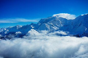 View above clouds in the mountains with high Alps peaks