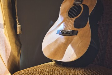 A Spanish acoustic classical guitar with steel and nylon strings resting on a chair next to a...
