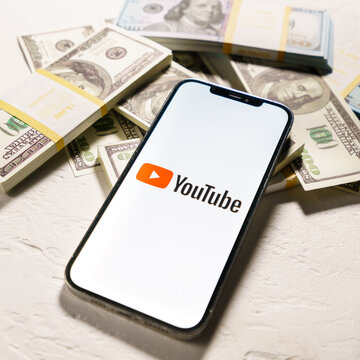 Berlin, Germany - February 02, 2022: Dollars banknotes and YouTube logo on the screen  iPhone 12 Pro Max. YouTube is a free video sharing application that