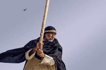 An old dangerous Arab in national clothes threatens with a stick.