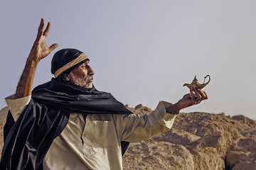 An old Arabic sorcerer holds an Aladdin's lamp and conjures.