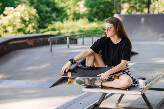 Female skater with a skateboard is sitting and resting in the skaters park