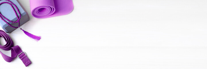 Accessories for yoga practice. Lavender yoga mat, foam block,mala beads and belt on lighnt background for banner copyspace.