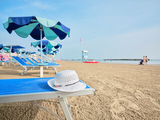 White straw hat on a beach bed with colorful umbrellas on a sunny summer day. In the background a...