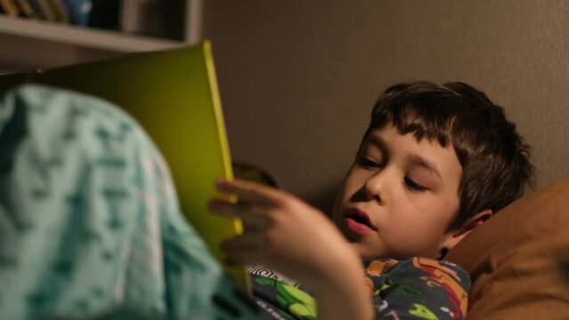 little boy reads a book on his own before going to bed.