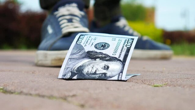 Close-up of a hundred dollar bill on the sidewalk and a walking man finds it