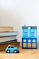 A blue toy car against the background of a plastic blue toy house and books stands on a wooden table.