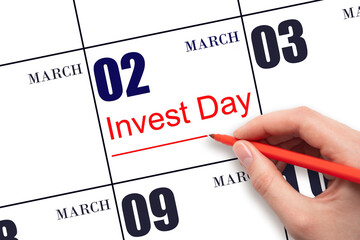 Hand drawing red line and writing the text Invest Day on calendar date March 2.  Business and financial concept.