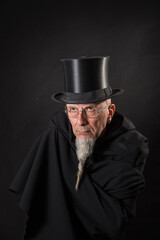 Portrait of a mysterious male magician in a black high top hat and black robe.