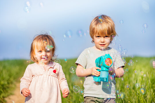 Toddler girl and blond boy brother play with soap bubble gun