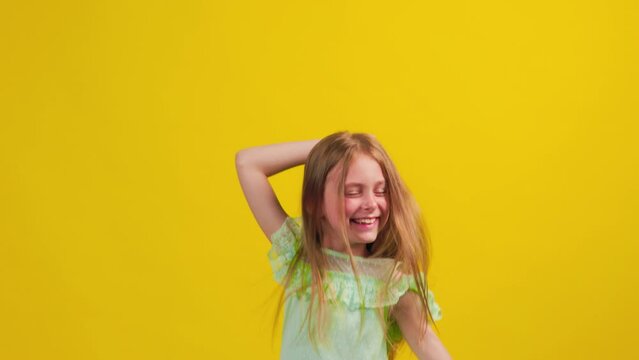 Happy kid girl in the blue dress jumping in studio. cute children dancing and jumping raising hands up. studio shot, yellow background