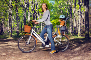 Mother with daughter ride city electric bike on park alley