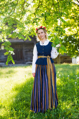 Latvian woman in traditional clothing posing on nature in village.