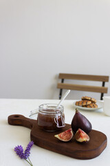 Homemade fig jam in the jar and fresh fig on the rustic wood board with cookies and milk jar on the background