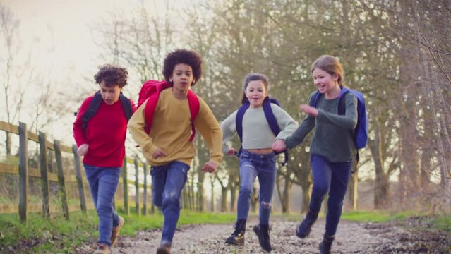 Portrait of children with school backpacks outdoors running towards camera along country lane - shot in slow motion