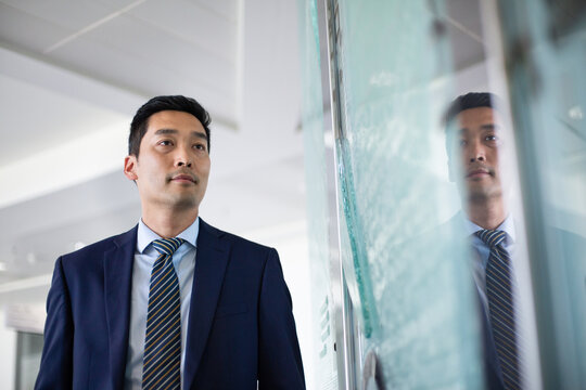 Asian businessman looking at reflection in a modern corporate office