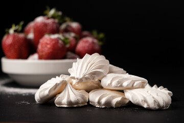 Meringue close up and strawberries in a plate on a black background. Fruit desserts.
