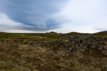 Fototapeta na wymiar Volcanic rocks, moss and sparse vegetations on a hill representing typical field in Iceland