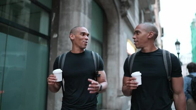 Two smiling bald African brothers talking and walking with cups of coffee on the street outdoors 
