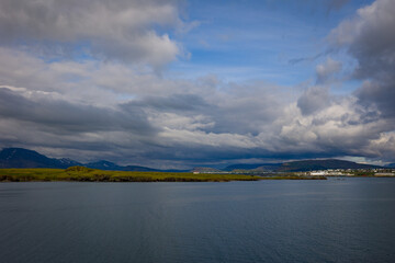 Dramatic skies over Reykjavik, Iceland harbor with snow covered mountains on the strip of land on the distance