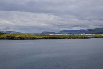 Clear and calm waters of Reykjavik harbor close to the city port. Icelandic mountain ranges displayed on the small strip of land in the middle of the frame.