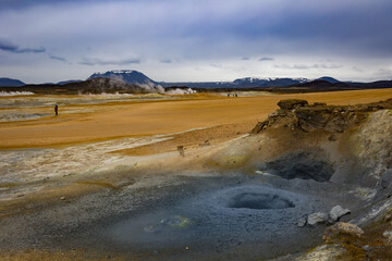 Bubbling mud pots site in Hverir, Iceland with a pile of volcanic rocks emitting sulphur gas. People walking on grounds that look like out of this world surface.