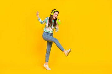 Fototapeta na wymiar Full body image of overjoyed carefree female dancing singing her favorite song isolated on yellow color background