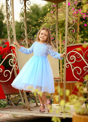 Cute little caucasian girl in a blue dress near the red carriage in the style of a princess. Summer. Parks.Childhood concept.