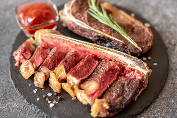 Grilled New York beef steak on the bone, herbs and spices on a stone background