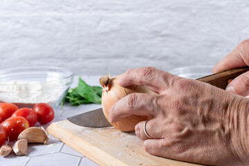A hand cutting onion between ingredients and kitchen tools.