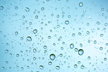 Rain outside the window. Water droplets on a car glass on a background of blue sky and green grass. Overcast. Wet clean nature, ecology