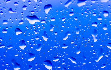 Rain outside the window. Water droplets on a car glass on a background of blue sky and green grass. Overcast. Wet clean nature, ecology