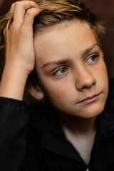 Portrait of blonde teenage boy on dark background outdoor. Low key close up shot of a young teen boy, adolescence. Selective focus. Loneliness, sadness, adolescent anxiety, emotional