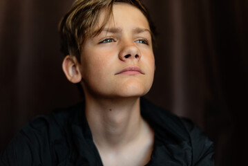 Portrait of blonde teenage boy on dark background outdoor. Low key close up shot of a young teen boy, adolescence. Selective focus. Loneliness, sadness, adolescent anxiety, emotional