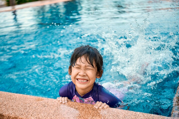 Happy Asian little girl enjoys swimming in outdoor swimming pool on hot summer day.