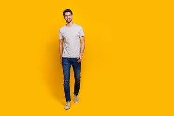 Full body photo of nice brunet millennial guy go wear t-shirt jeans shoes isolated on yellow background