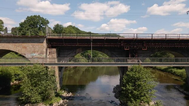 Young caucasian man standing on the footpath of an old rusty train trestle in Germany during spring. Wide angle aerial pull away shot