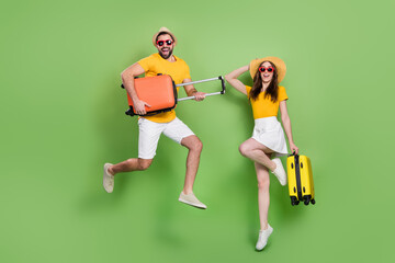 Fototapeta na wymiar Full size photo of two excited energetic people jumping hold suitcase isolated on green color background