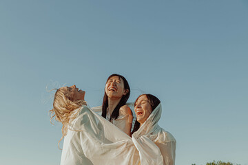 THREE HAPPY GIRLS ARE PLAYING WITH A FABRIC.