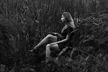 Beautiful woman with a gun sitting among reeds in black and white