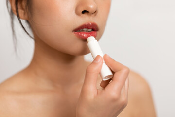 Cropped of korean lady using lipbalm, taking care of her beautiful lips, putting hygienic lipstick,...