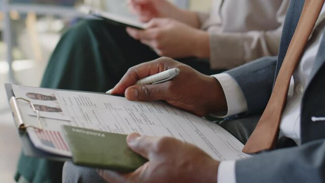 Close up tilt up shot of African American man in formal suit filling out visa application form before interview in embassy