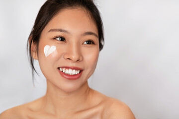 Facial skincare. Happy korean lady with heart-shaped moisturizer cream on face posing over white background, copy space