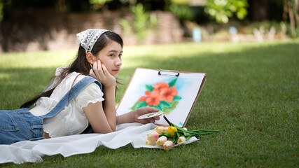 Charming Girl woman sitting on plaid at the park in sunny summer day and using watercolor for...