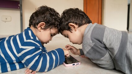 twin children playing with the cell phone on the floor of their home