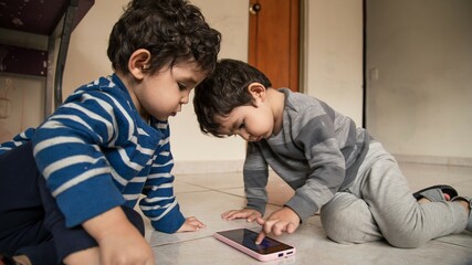 twin children playing with the cell phone on the floor of their home